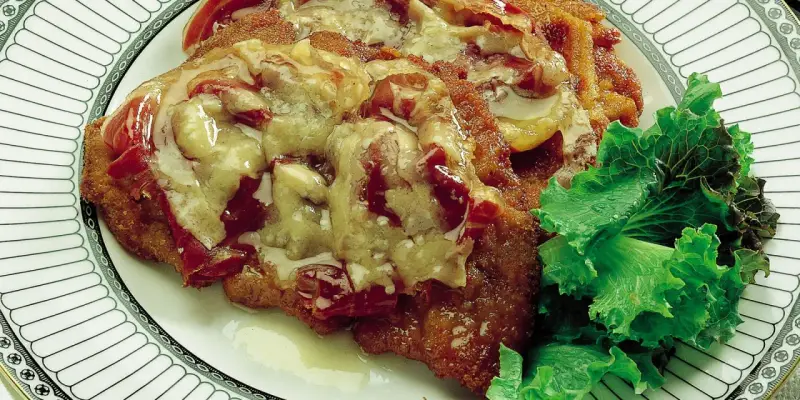 Cotoletta alla bolognese ricoperta di sugo e formaggio fuso, servita con insalata fresca su un piatto decorato.
